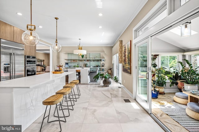 kitchen featuring ornamental molding, appliances with stainless steel finishes, decorative light fixtures, and a breakfast bar area