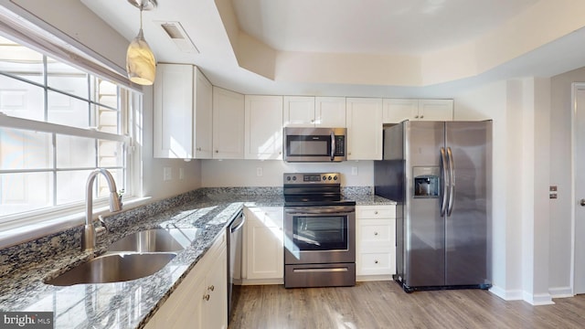 kitchen featuring appliances with stainless steel finishes, hanging light fixtures, stone counters, sink, and white cabinetry