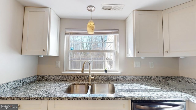 kitchen featuring stainless steel dishwasher, sink, white cabinetry, and stone countertops