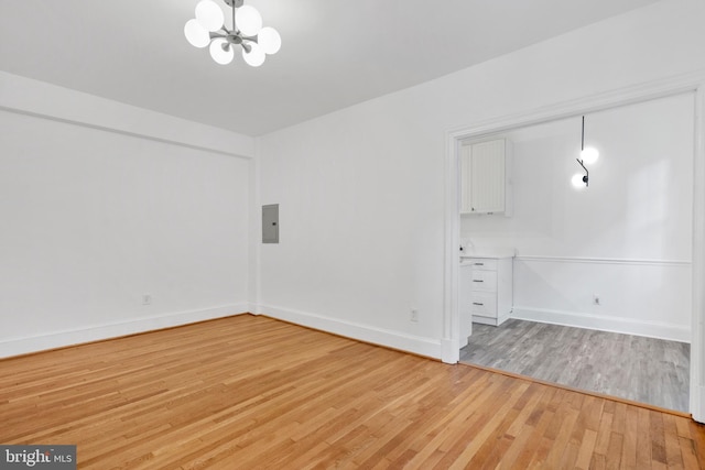 empty room featuring electric panel, light hardwood / wood-style floors, and a notable chandelier