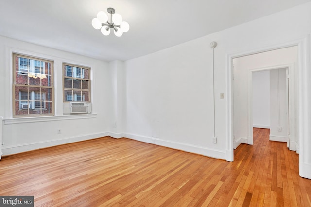 empty room featuring cooling unit, light hardwood / wood-style flooring, and a notable chandelier