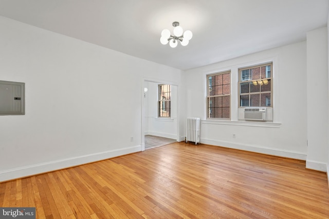 unfurnished room featuring radiator, cooling unit, electric panel, and light wood-type flooring