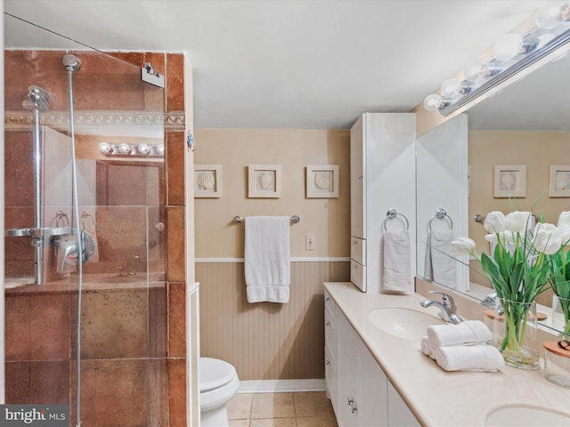 bathroom with tiled shower, toilet, vanity, wooden walls, and tile patterned flooring