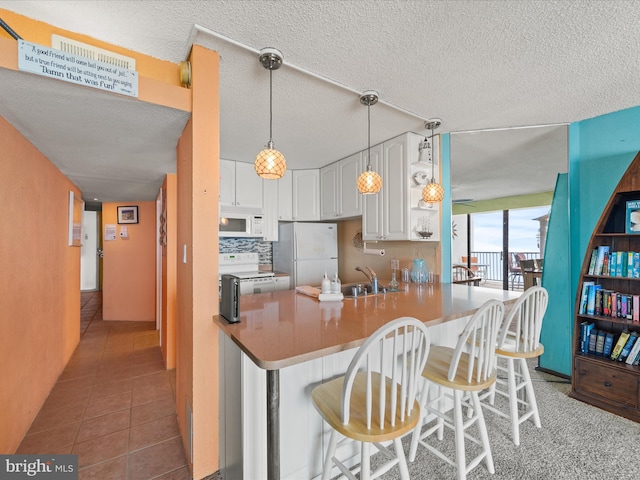 kitchen with white appliances, a breakfast bar, dark tile patterned floors, white cabinetry, and kitchen peninsula