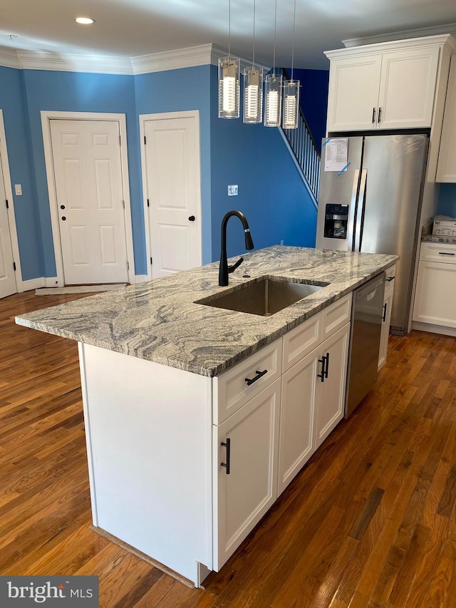 kitchen with hanging light fixtures, stainless steel appliances, white cabinets, sink, and a kitchen island with sink