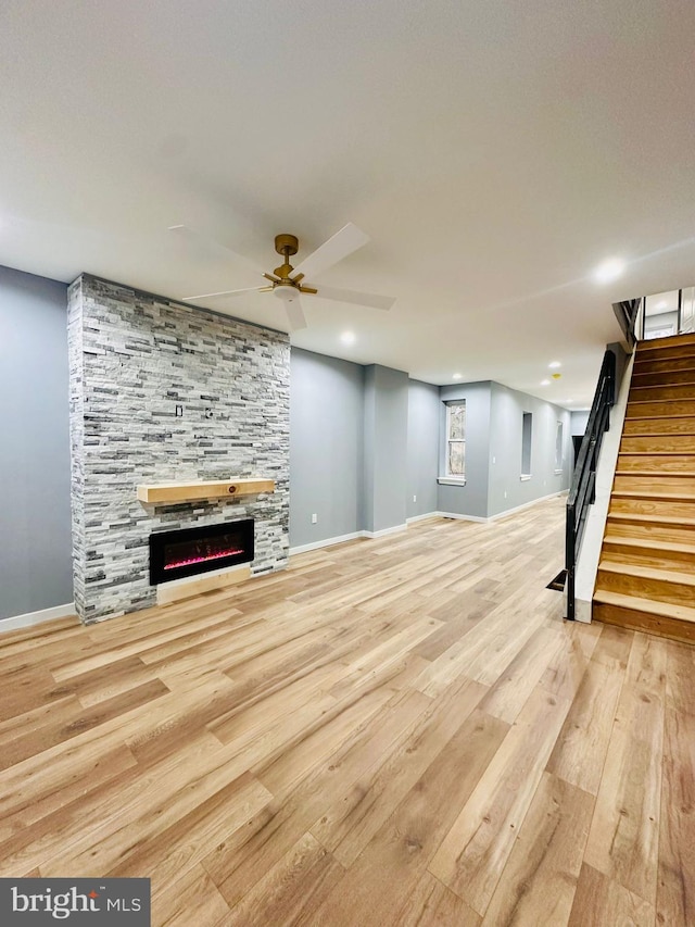 unfurnished living room featuring ceiling fan, a stone fireplace, and light hardwood / wood-style floors