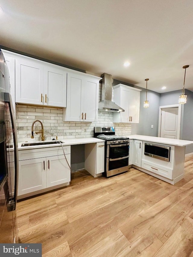 kitchen featuring white cabinetry, decorative light fixtures, wall chimney exhaust hood, and appliances with stainless steel finishes