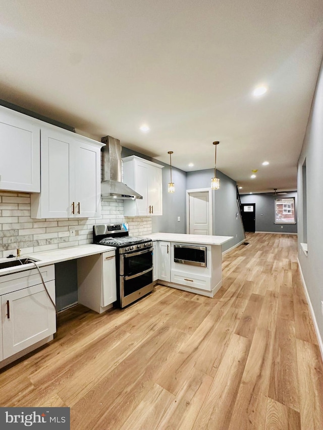 kitchen with white cabinetry, hanging light fixtures, kitchen peninsula, stainless steel appliances, and wall chimney range hood