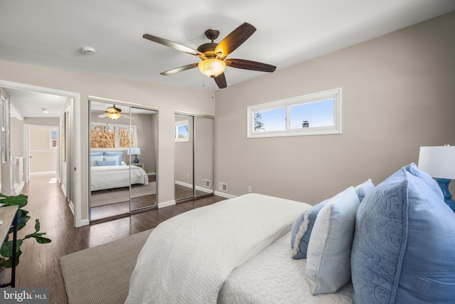 bedroom with ceiling fan, dark wood-type flooring, and multiple closets