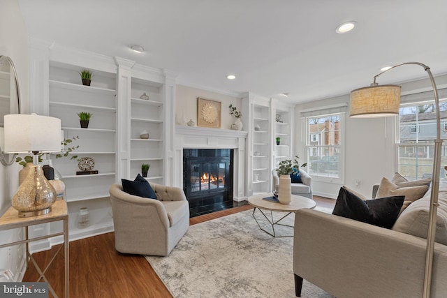 living room featuring wood finished floors, a fireplace with flush hearth, built in features, and recessed lighting