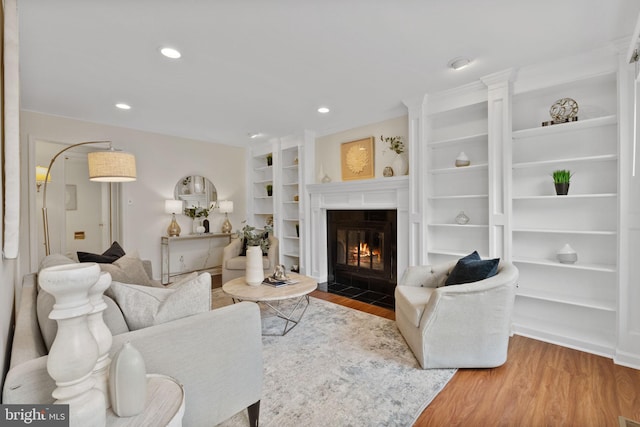 living area featuring a fireplace with flush hearth, built in shelves, wood finished floors, and recessed lighting