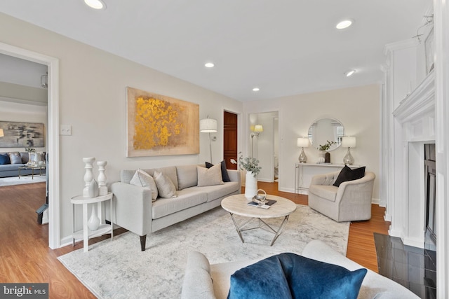 living room featuring recessed lighting, a fireplace with raised hearth, baseboards, and wood finished floors