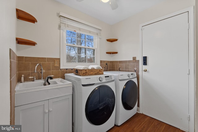 laundry area featuring tile walls, washing machine and clothes dryer, cabinet space, a sink, and wood finished floors