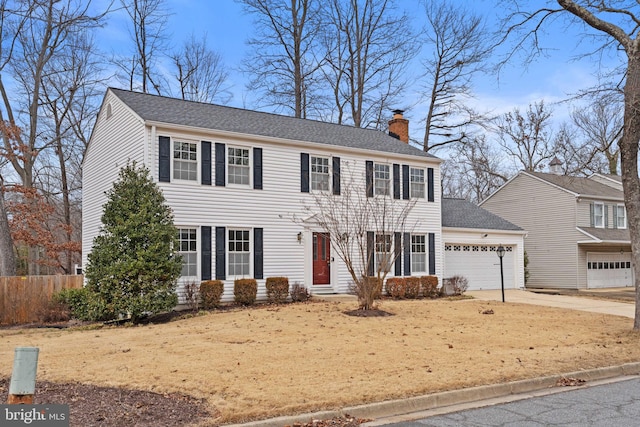 colonial house featuring driveway, a shingled roof, a chimney, an attached garage, and fence