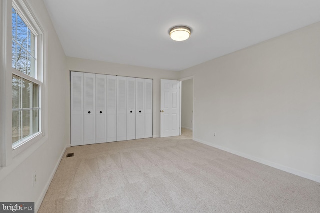 unfurnished bedroom featuring multiple windows, carpet flooring, visible vents, and baseboards