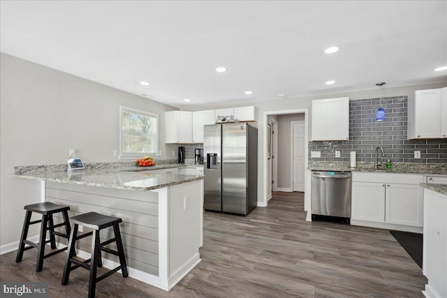 kitchen with appliances with stainless steel finishes, decorative light fixtures, white cabinetry, kitchen peninsula, and light stone countertops