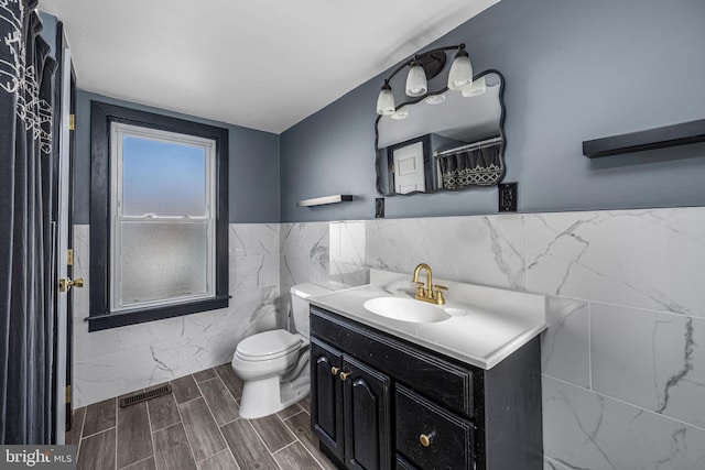 bathroom with walk in shower, vanity, toilet, and tile walls