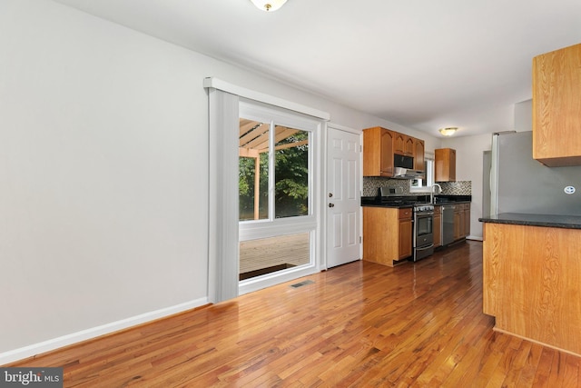 11501 Piney Lodge Rd, North Potomac, MD 20878 - kitchen with appliances with stainless steel finishes, wood finished floors, decorative backsplash, under cabinet range hood, and dark countertops