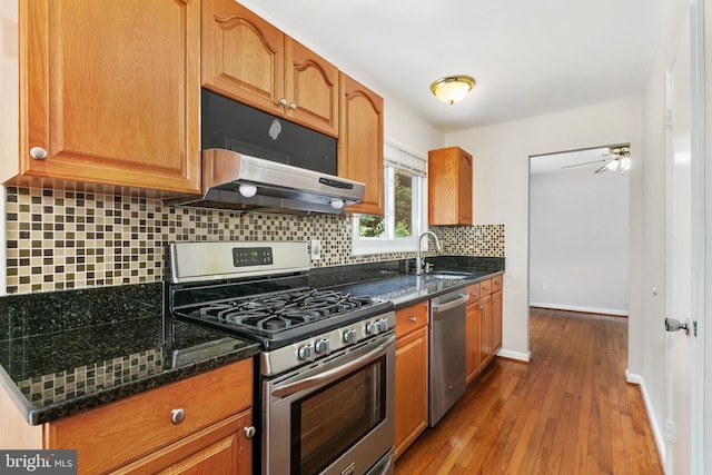 11501 Piney Lodge Rd, North Potomac, MD 20878 - kitchen with appliances with stainless steel finishes, a sink, under cabinet range hood, dark wood-type flooring, and decorative backsplash