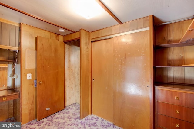 unfurnished bedroom with light carpet, wooden walls, and a closet