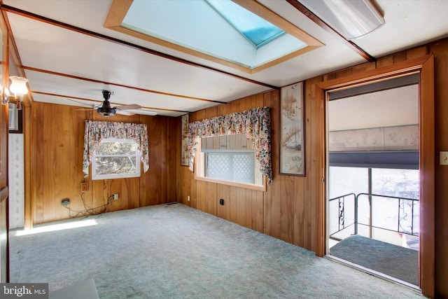 unfurnished room featuring ceiling fan, carpet flooring, a skylight, and wood walls