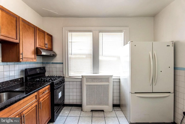 kitchen featuring dark stone countertops, plenty of natural light, black gas stove, and white fridge