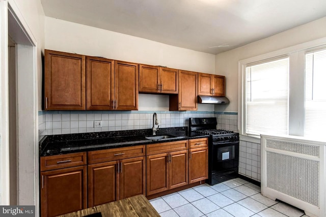 kitchen featuring dark stone countertops, radiator, sink, and black gas stove