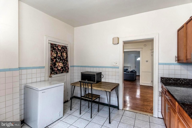 kitchen featuring fridge, dark stone countertops, tile walls, and light tile patterned floors