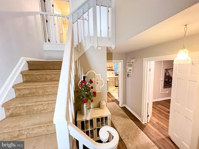 staircase with a towering ceiling and wood-type flooring