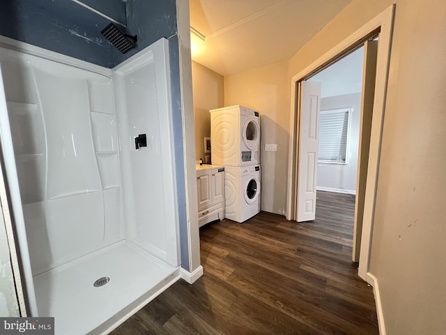 bathroom with hardwood / wood-style flooring, vanity, stacked washing maching and dryer, and a shower