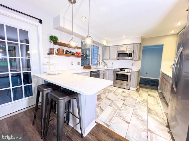 kitchen featuring appliances with stainless steel finishes, a breakfast bar, gray cabinetry, and kitchen peninsula