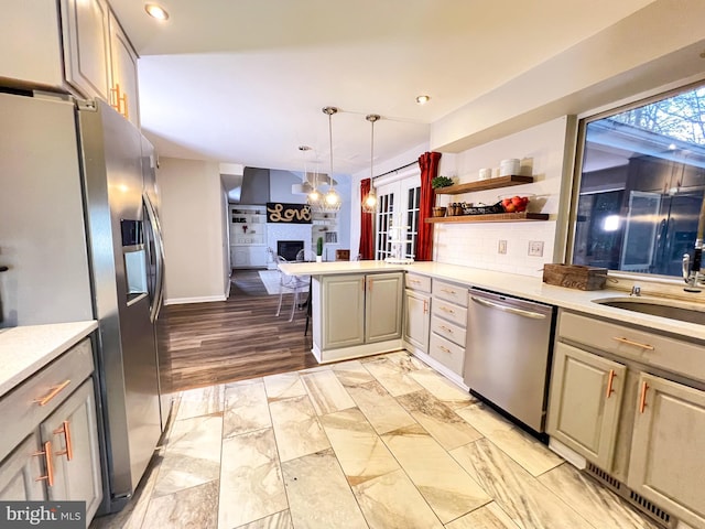 kitchen with appliances with stainless steel finishes, decorative light fixtures, sink, backsplash, and kitchen peninsula