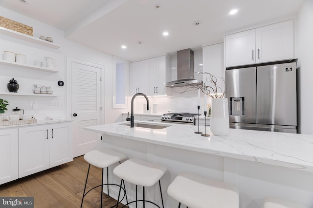 kitchen with sink, light stone counters, white cabinetry, stainless steel appliances, and wall chimney range hood