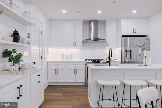 kitchen with stainless steel appliances, white cabinets, light stone counters, and wall chimney exhaust hood