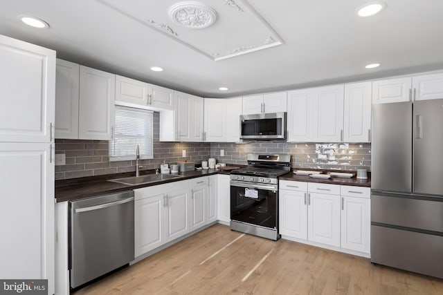 kitchen featuring sink, white cabinetry, tasteful backsplash, light wood-type flooring, and appliances with stainless steel finishes