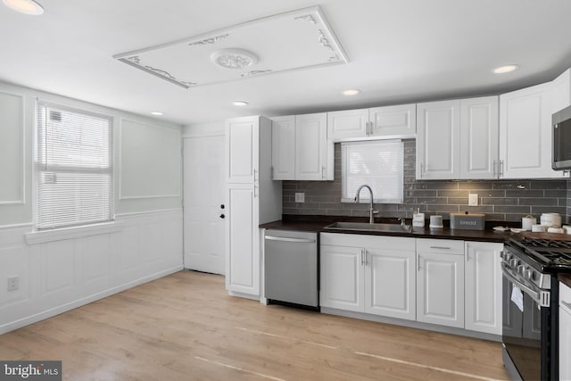 kitchen with appliances with stainless steel finishes, white cabinetry, sink, decorative backsplash, and light hardwood / wood-style floors