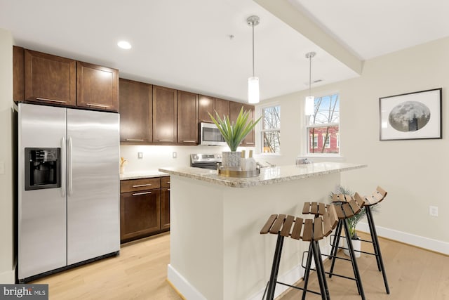 kitchen with appliances with stainless steel finishes, a center island, hanging light fixtures, and light hardwood / wood-style flooring