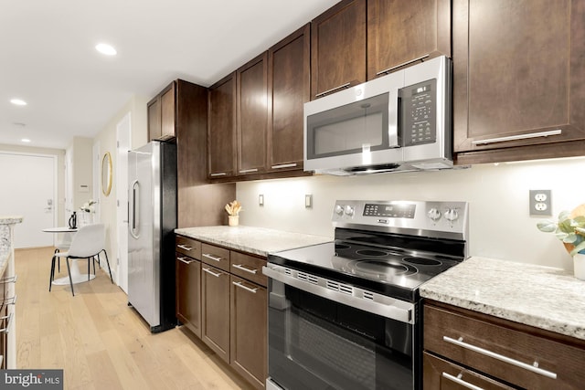 kitchen with appliances with stainless steel finishes, light wood-type flooring, light stone counters, and dark brown cabinets