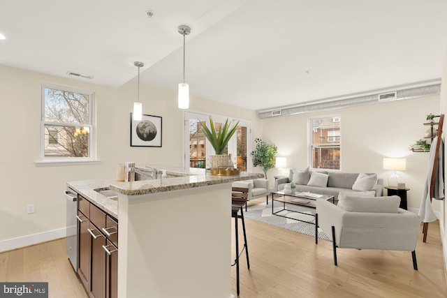 kitchen featuring sink, light hardwood / wood-style flooring, a breakfast bar area, hanging light fixtures, and light stone countertops