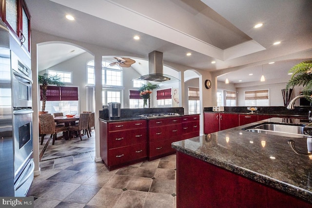 kitchen featuring island exhaust hood, sink, dark stone countertops, ceiling fan, and stainless steel appliances