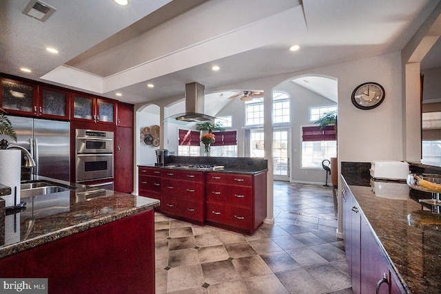 kitchen featuring island range hood, dark stone counters, ceiling fan, and appliances with stainless steel finishes