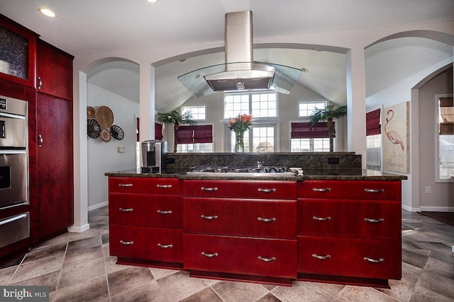 kitchen with vaulted ceiling, appliances with stainless steel finishes, dark stone counters, and island exhaust hood