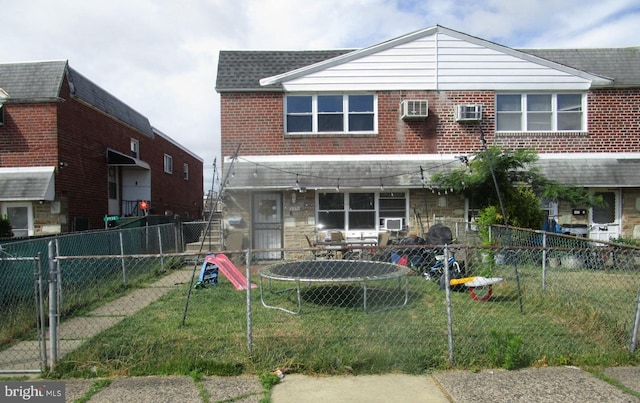 back of house with a yard, a wall mounted air conditioner, and a trampoline