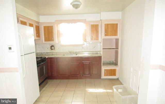 kitchen featuring sink, backsplash, white refrigerator, light stone counters, and gas stove