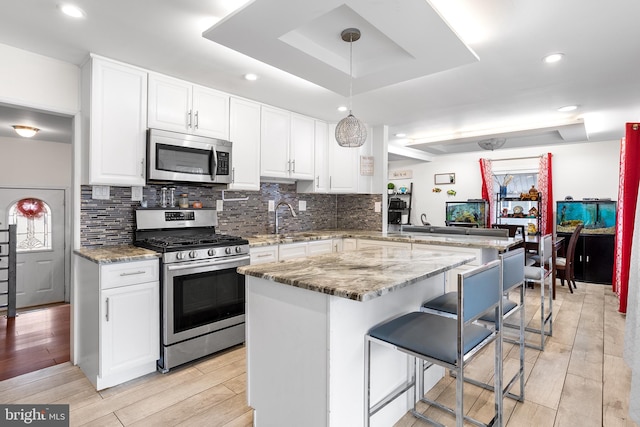 kitchen with appliances with stainless steel finishes, hanging light fixtures, a tray ceiling, a kitchen bar, and kitchen peninsula