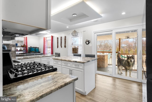 kitchen featuring pendant lighting, gas cooktop, white cabinetry, a center island, and light stone counters