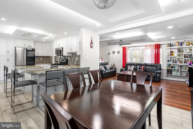 dining room featuring ceiling fan, a raised ceiling, and light wood-type flooring