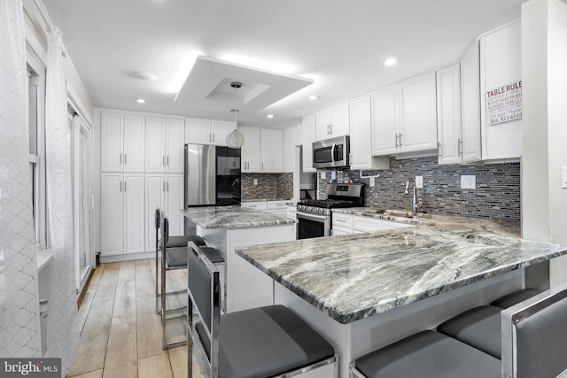 kitchen featuring stainless steel appliances, white cabinetry, light stone countertops, and a kitchen breakfast bar