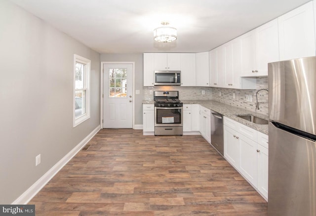 kitchen with sink, appliances with stainless steel finishes, white cabinets, light stone countertops, and backsplash