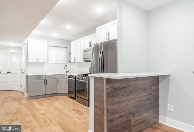 kitchen featuring white cabinetry, sink, decorative backsplash, stainless steel appliances, and light wood-type flooring